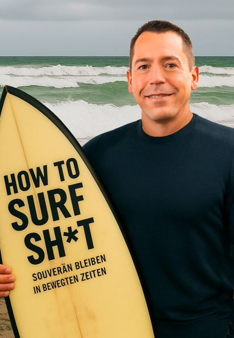 Jan Michael Rasimus steht mit Surfbrett am Strand. Auf dem Surfbrett steht How to Surft Sh*t.