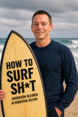 Jan Michael Rasimus steht mit Surfbrett am Strand. Auf dem Surfbrett steht How to Surft Sh*t.